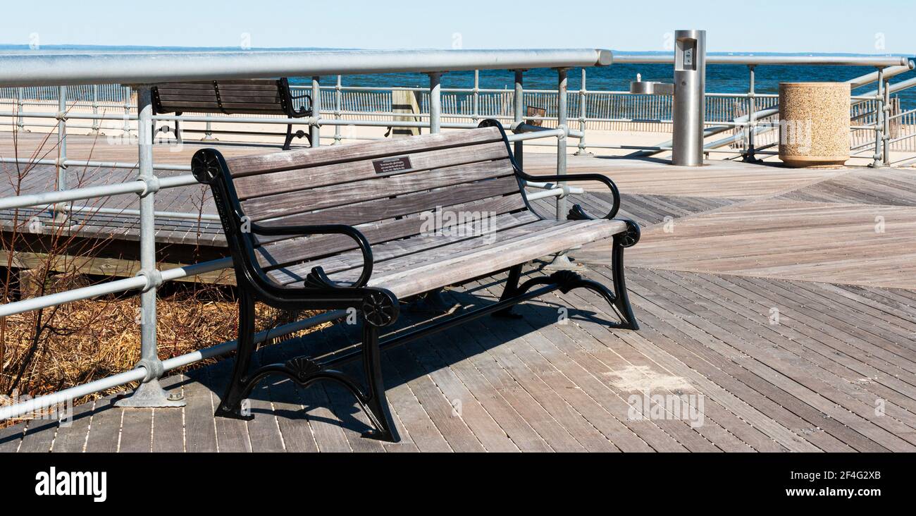 A park bench with a dedicated name plate on the boardwalk at Sunken Meadow State Park on a sunny March morning with the beach in the background. Stock Photo