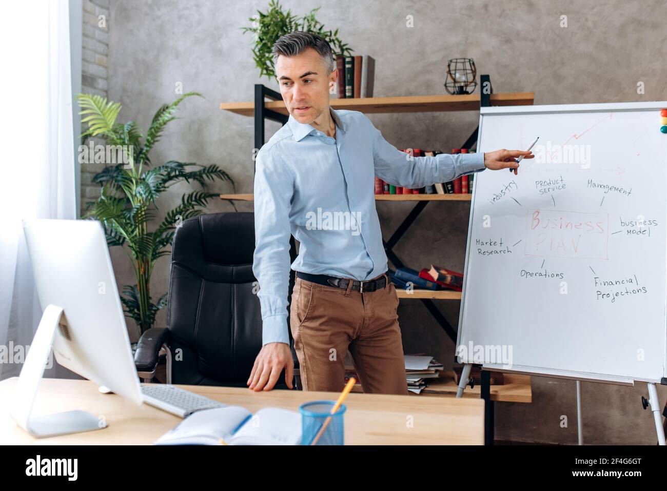 Serious influential modern caucasian middle aged ceo or manager, conducts online briefing for coworkers via video conference, shows a presentation about company business plan on a flipchart Stock Photo