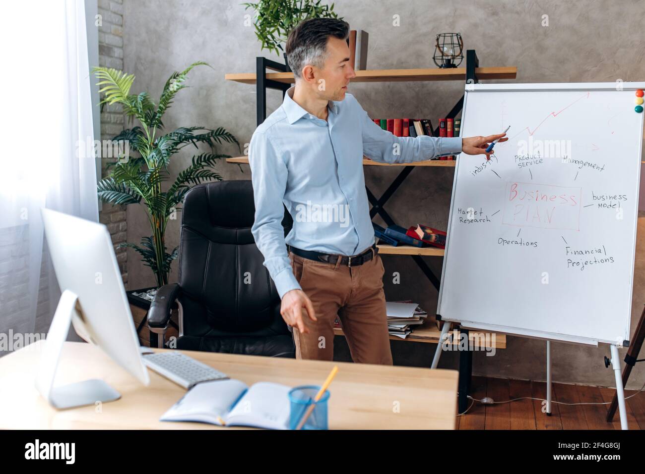 Successful confident caucasian middle aged businessman or manager, conducts online briefing for coworkers via video conference, shows a presentation about company business plan on a flipchart Stock Photo