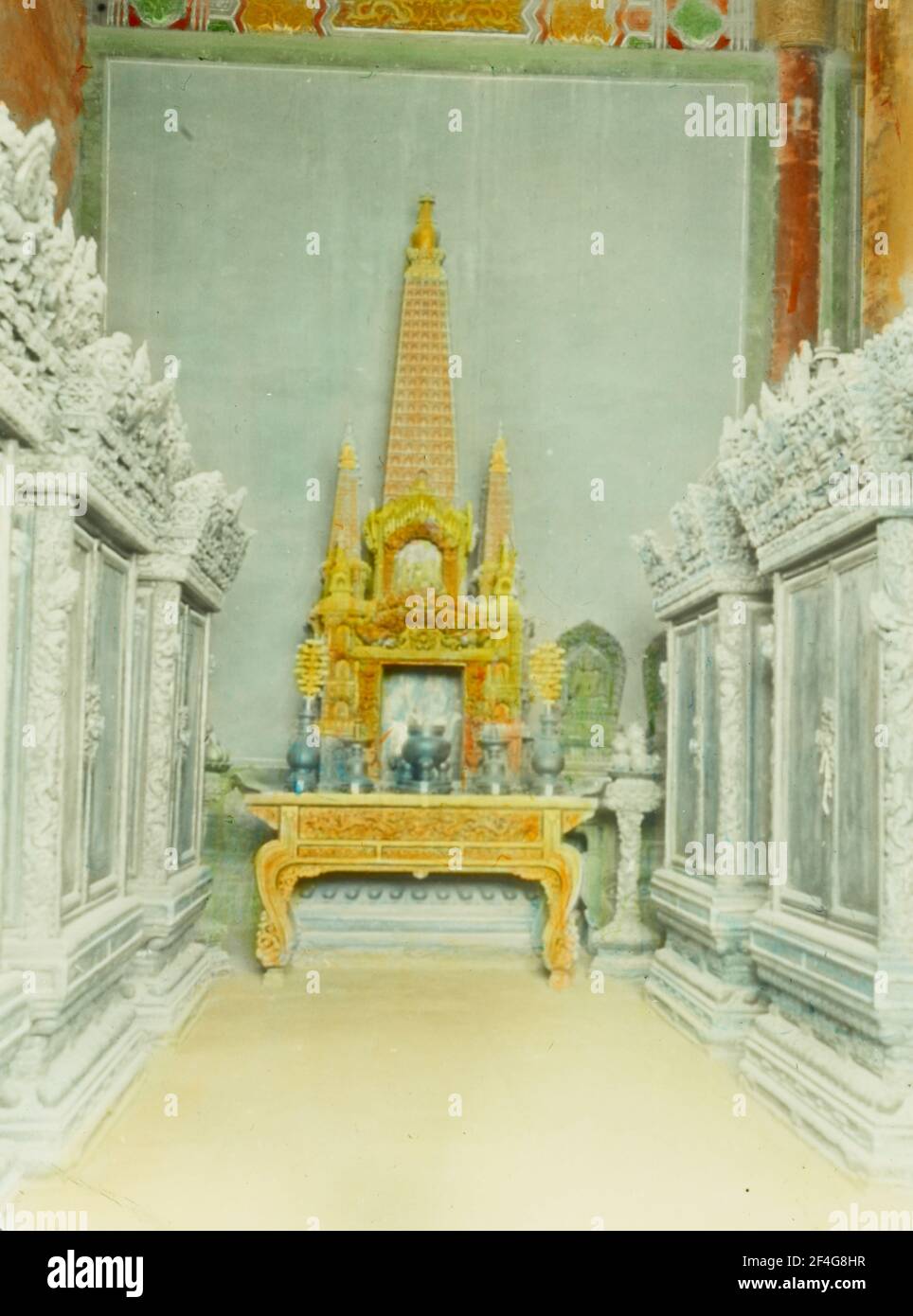 Frontal view of a low, gilded Buddhist altar, with pagoda-like spires and receptacles for offerings on its surface, placed against a wall and hemmed by ornately carved cabinets, Beijing, China, 1918. From the Sidney D. Gamble photographs collection. () Stock Photo