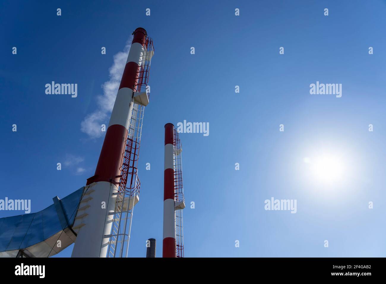 Smoke Coming Out from Industrial Power Plant Chimneys. District Heating Plant Exterior With Industrial Chimneys Against the Sun and Blue Sky. Stock Photo