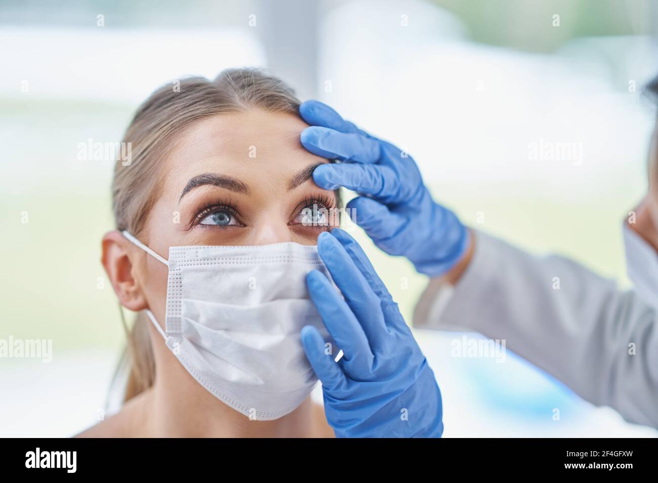 Eye-doctor in mask checking up on female patient Stock Photo