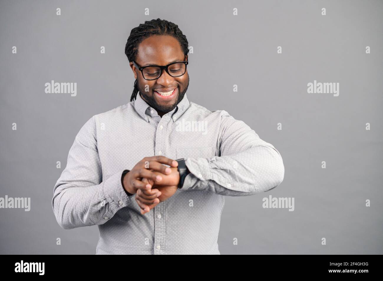 Punctual Afro American businessman in good mood, standing, checking his smartwatch, received notification, checks the pulse using modern device, keeps track of time while going to a meeting or date Stock Photo