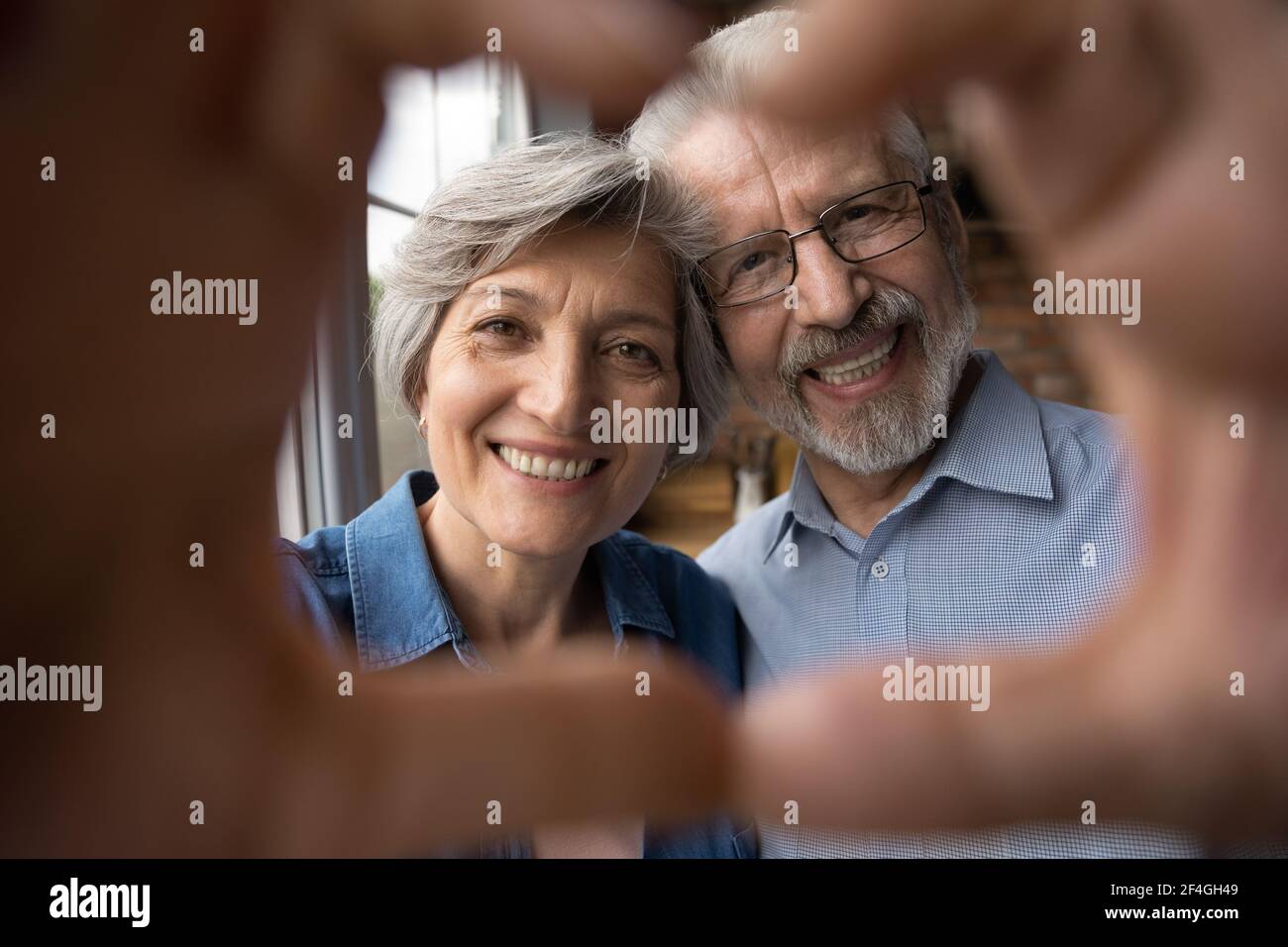 Smiling old age couple unite fingers before camera in heart Stock Photo