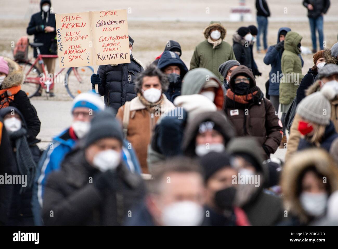 Munich, Germany. 21st Mar, 2021. During a rally of the organization 'GemeinsamZukunft' against the lockdown on the Theresienwiese, a demonstrator holds a sign with the inscription 'Why no masks, no vaccine, no Amazon tax? Grundrechte kassiert dafür, Gastro/Kneipen Künsterl Handel ruiniert' in the hands. The participants of the rally want to protest peacefully with distance and FFP2 masks against the lockdown. Credit: Matthias Balk/dpa/Alamy Live News Stock Photo