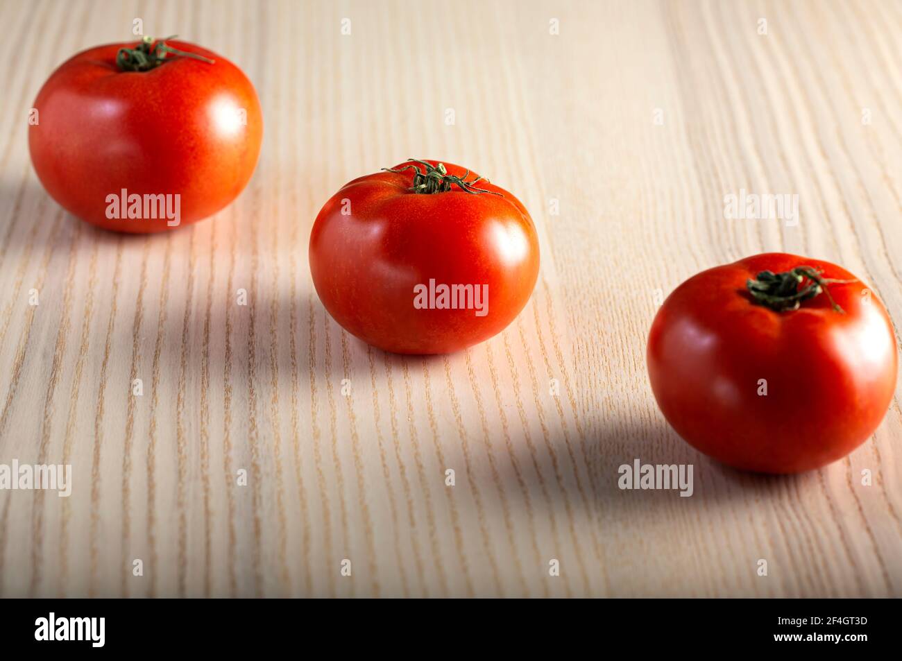 Three organic tomatoes on a wooden table Stock Photo