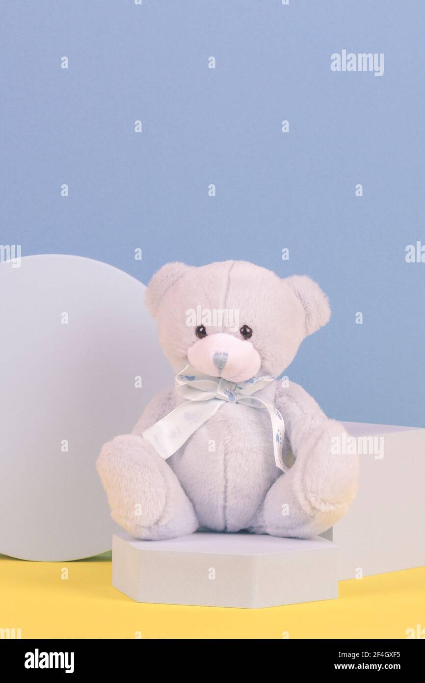 Baby kid toy background. Blue teddy bear and geometric shapes podium platform on light blue and yellow background Stock Photo