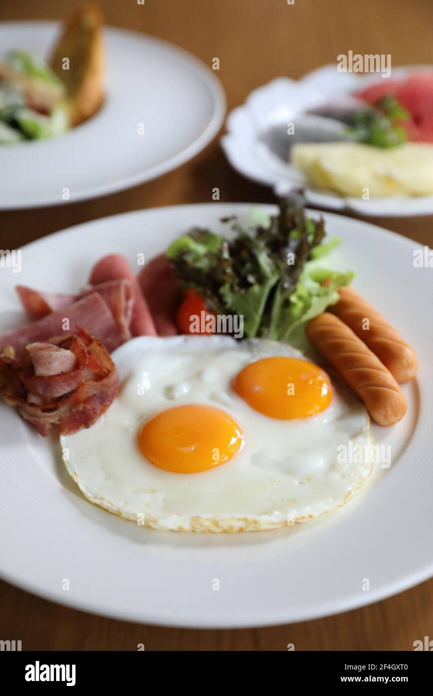 Breakfast set with fried eggs, bacon, sausages, beans, toasts, fresh salad and fruit on wood table Stock Photo