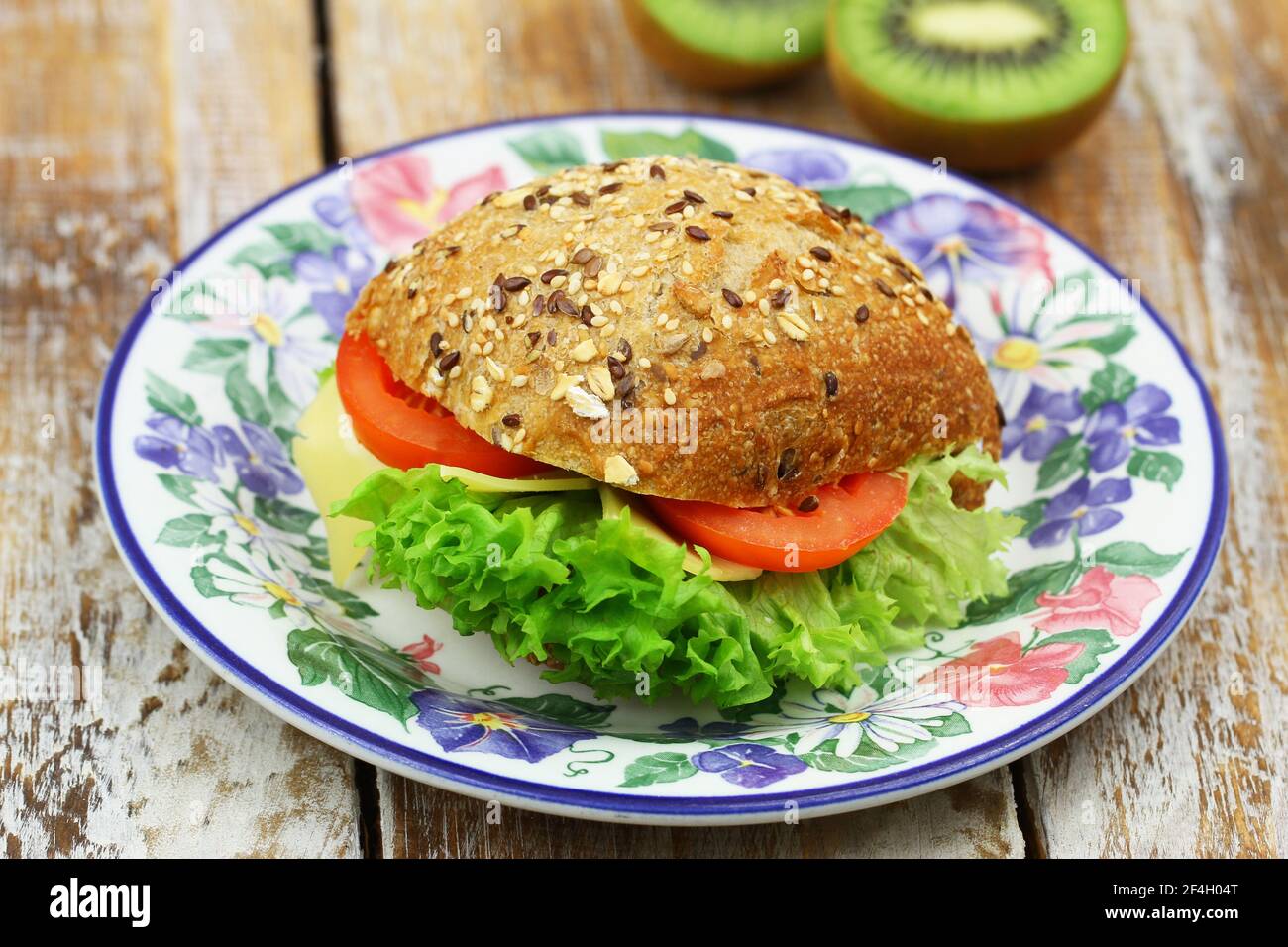 Mixed grain roll with cheese, lettuce and tomato on colorful vintage plate Stock Photo