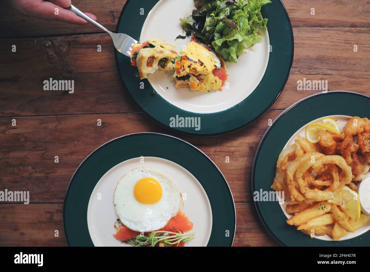 Meal egg benedict , fish and chips and zucchini fritters on top view with man hand wood background Stock Photo