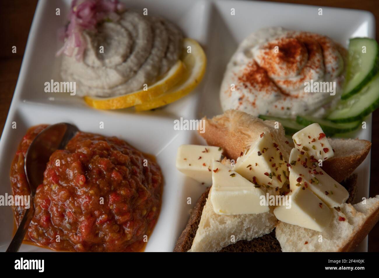 Closeup of butter pieces with spicy seasonings. White crockery plate with mezze tasting set of assorted pate pastes and appetizers with bread toasts. Stock Photo