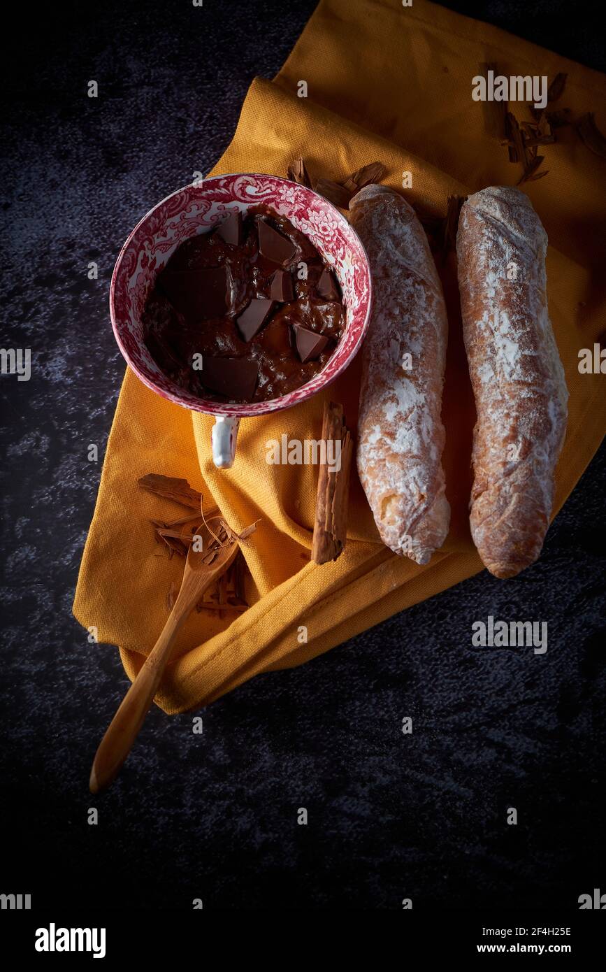 Fartons, typical pastries from Valencia, Spain, with hot chocolate, in a  Chinese ceramic container on top of a yellow cloth, with a dark surface. A  sw Stock Photo - Alamy