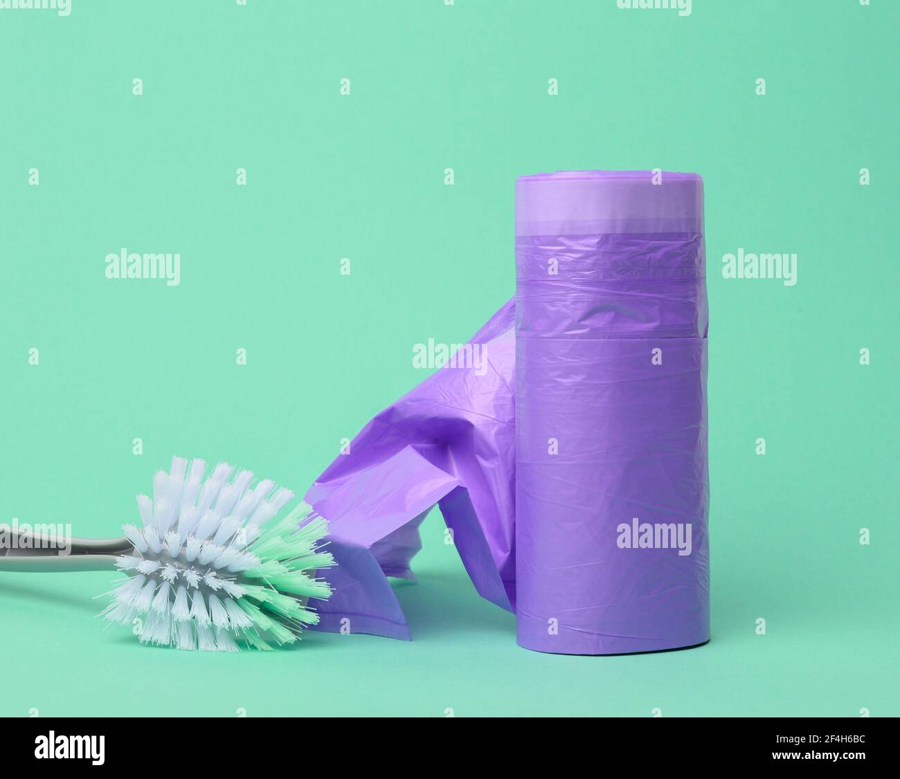 plastic brush and skein of purple plastic trash bags with strings on a green background, close up Stock Photo