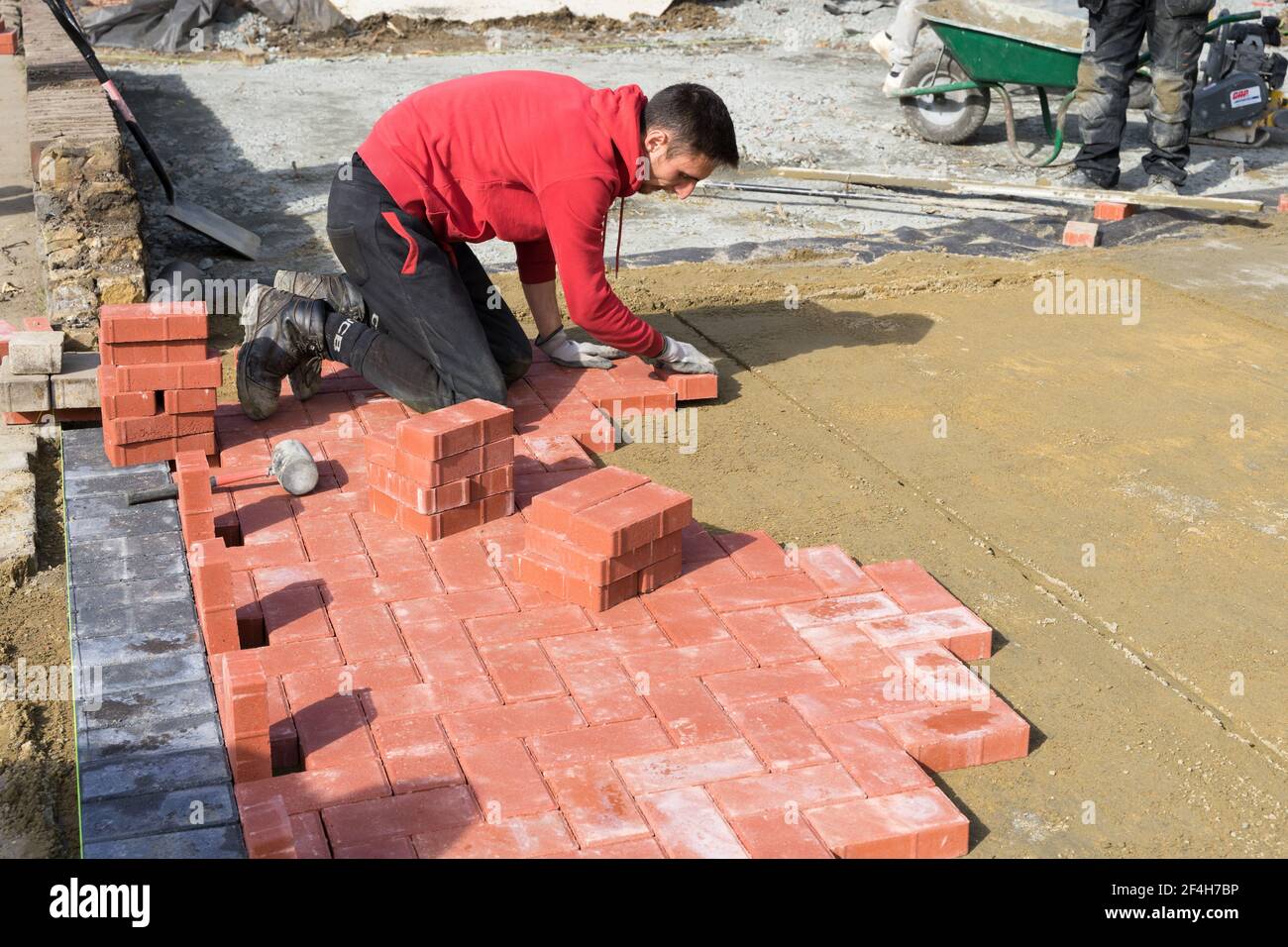 Paver lays paving bricks on top of base sand layer under a sunny day, England Stock Photo