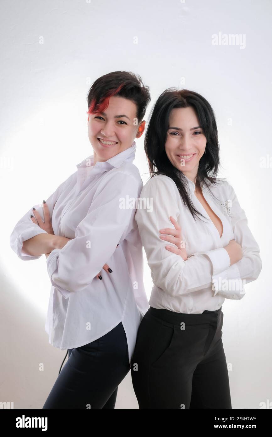 Portrait of two laughing women dressed in white clothes standing back to back isolated over white background Stock Photo