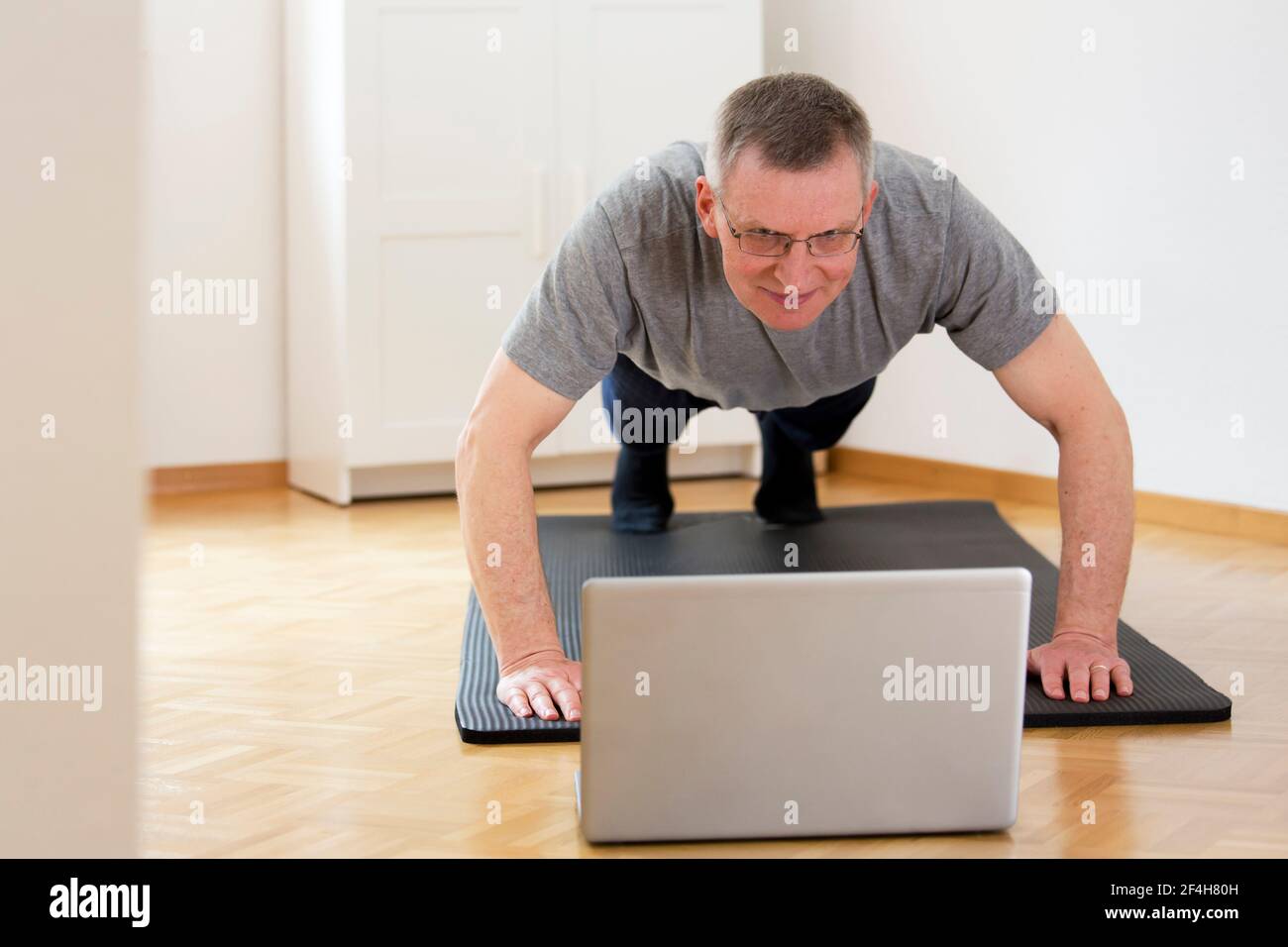 Mature or senior man doing push ups at home in front of laptop - focus on the face Stock Photo