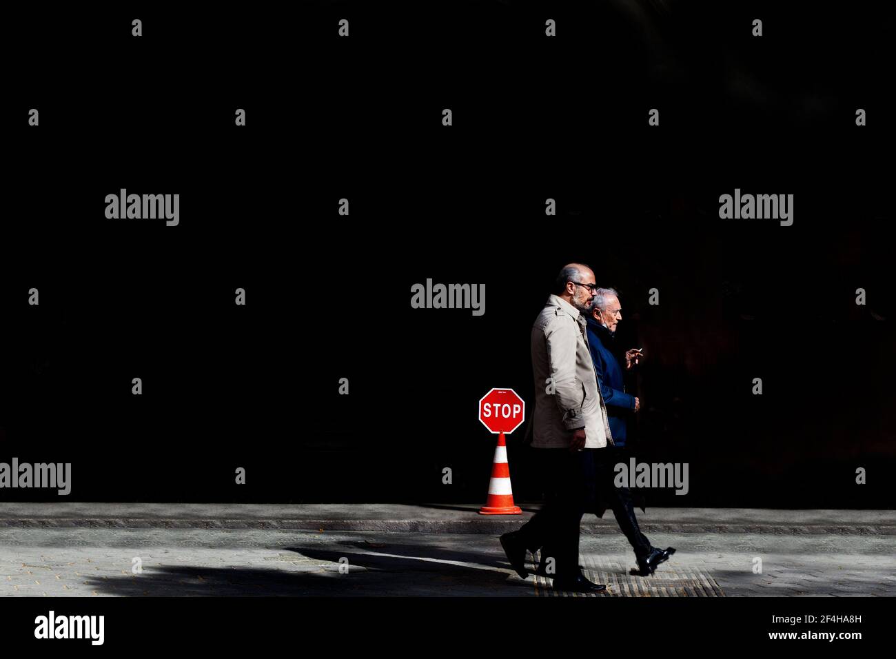 Two men smoking walking past Stop sign. Stock Photo