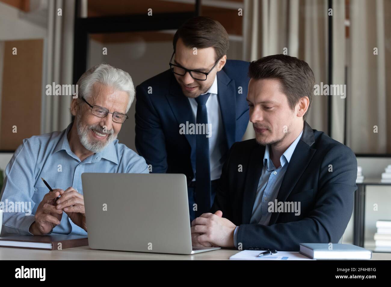 Smiling male colleagues cooperate at laptop discussing ideas Stock Photo