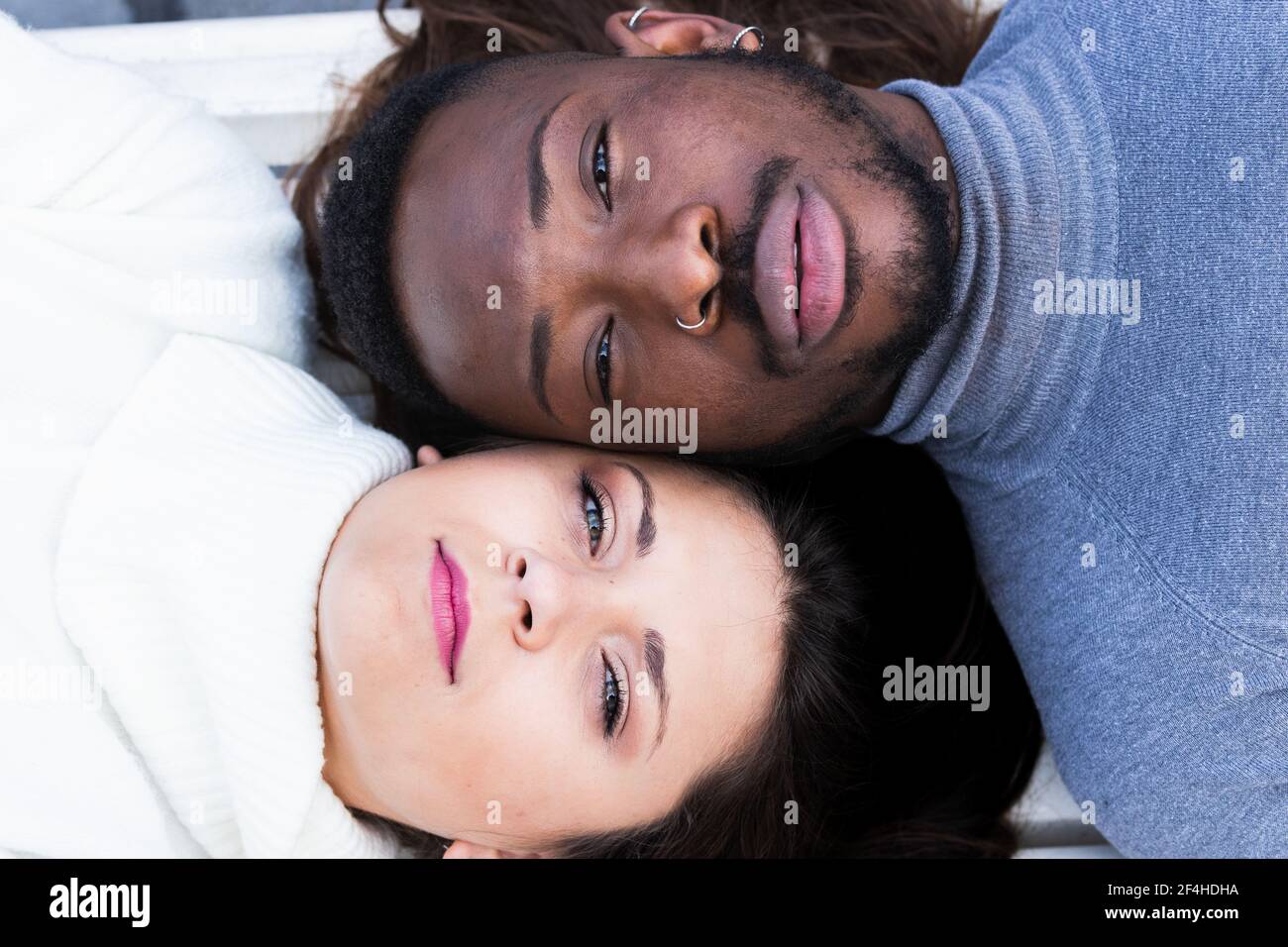 From above closeup of crop young multiracial couple lying face to face and looking at camera while enjoying romantic time together Stock Photo