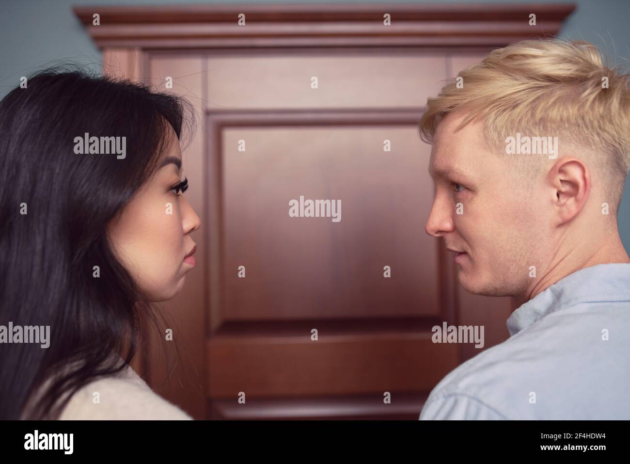 Side view of multiethnic couple sitting in office of psychologist and looking at each other while solving relationship problems together during mental Stock Photo