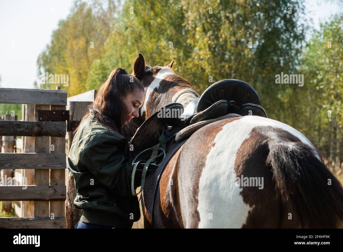 Cute girl gets ready for a ride on a horse and saddles it on an autumn day Stock Photo