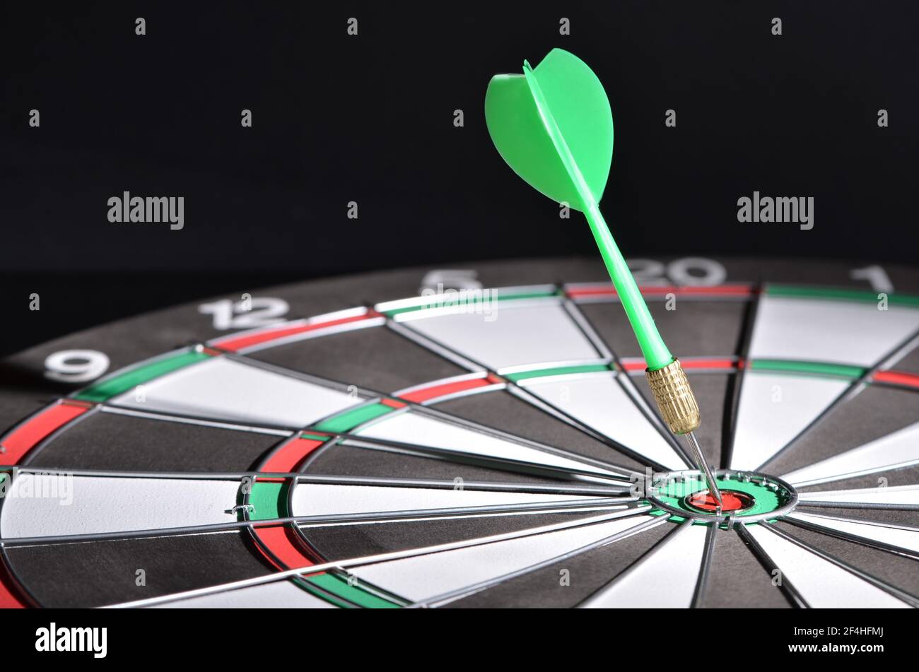 A green dart hitting the bullseye on the dartboard. Selective focus