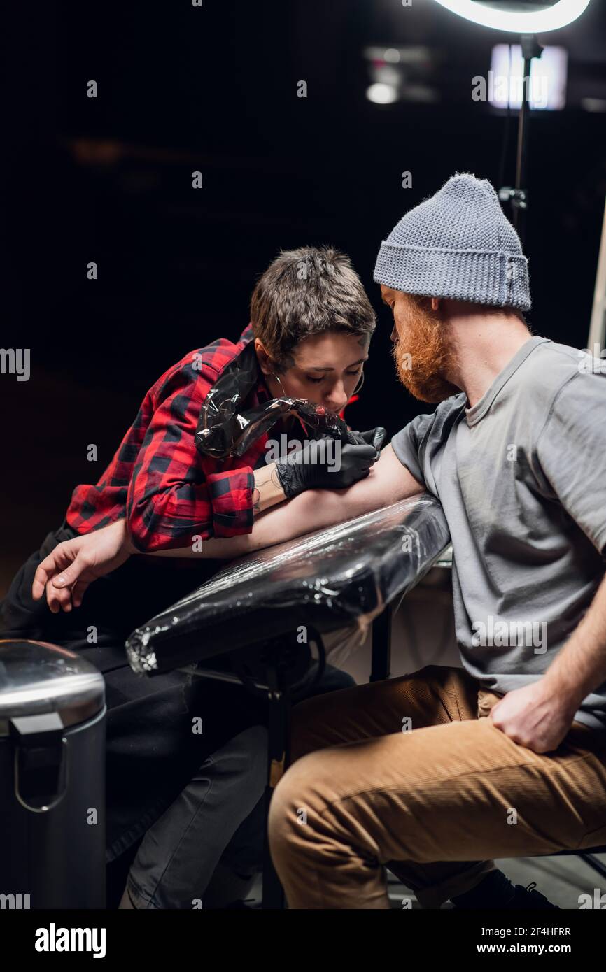 In a modern tattoo parlor, a girl with piercings and tattoos on her body makes a tattoo on the