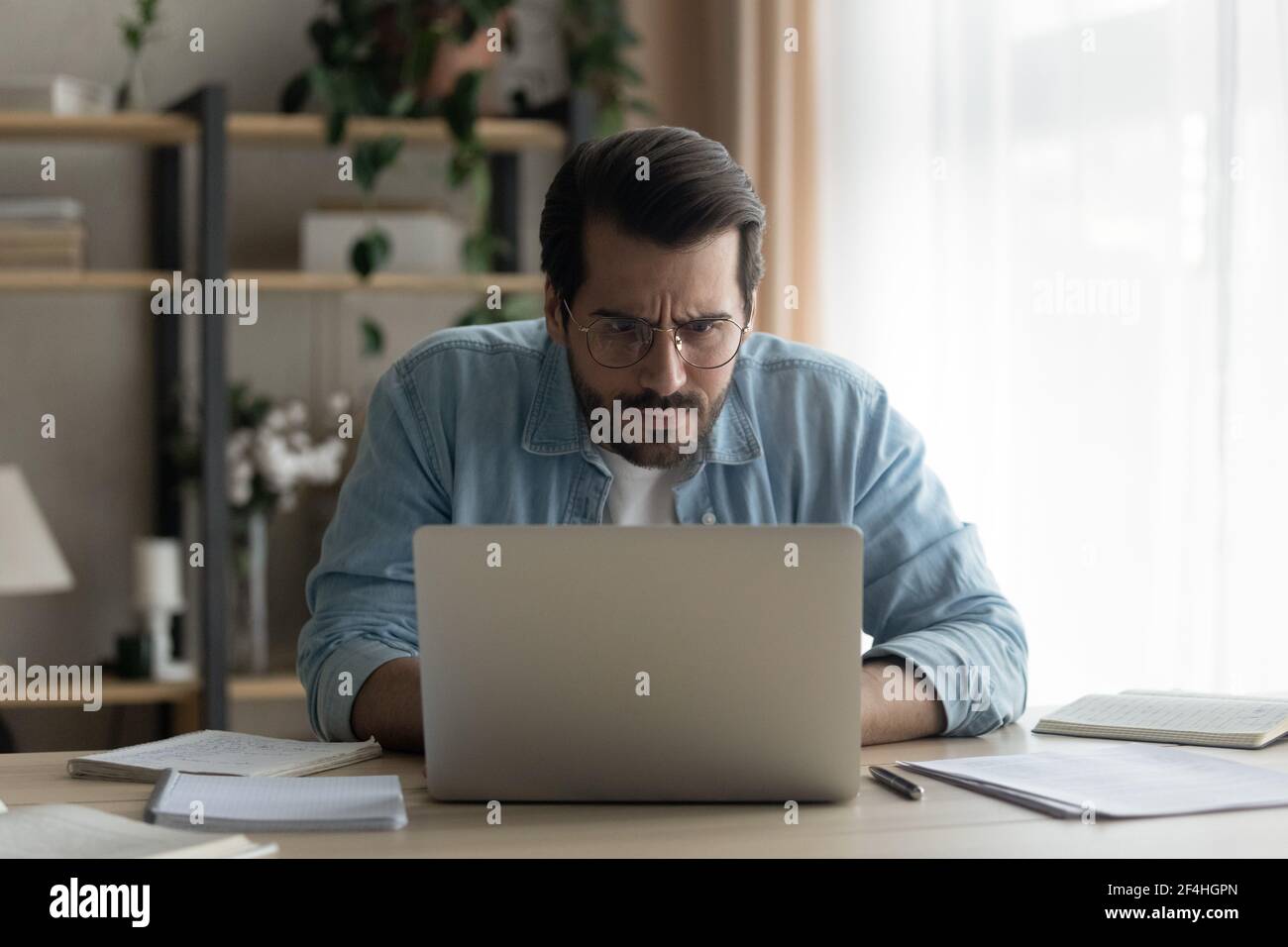 Close up puzzled businessman wearing glasses looking at laptop screen Stock Photo