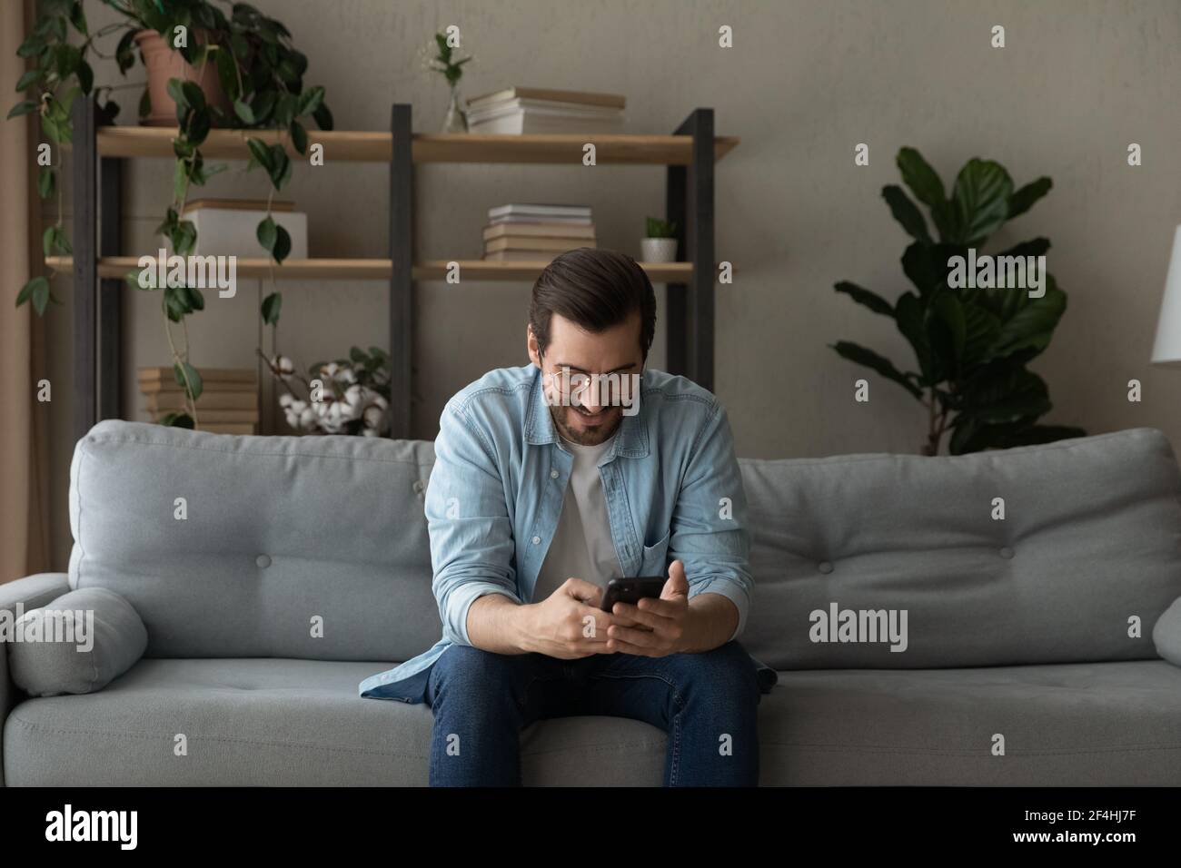 Smiling man wearing glasses having fun with phone at home Stock Photo