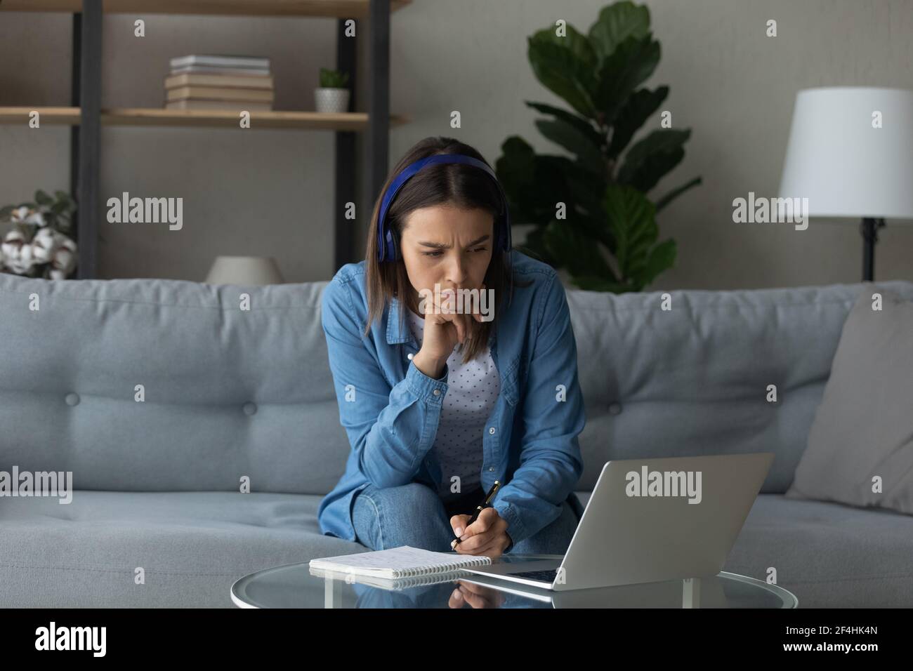 Focused woman wearing headphones looking at laptop screen, taking notes ...