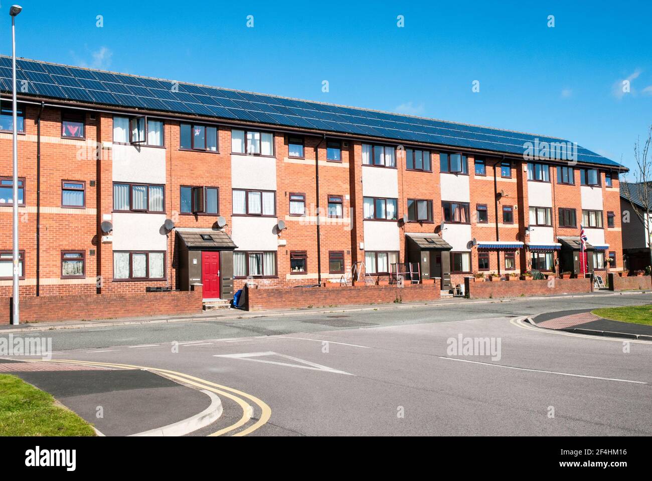 A large three storey block of flats with the roof covered with south facing solar panels to produce enviromental friendly power to flats Stock Photo