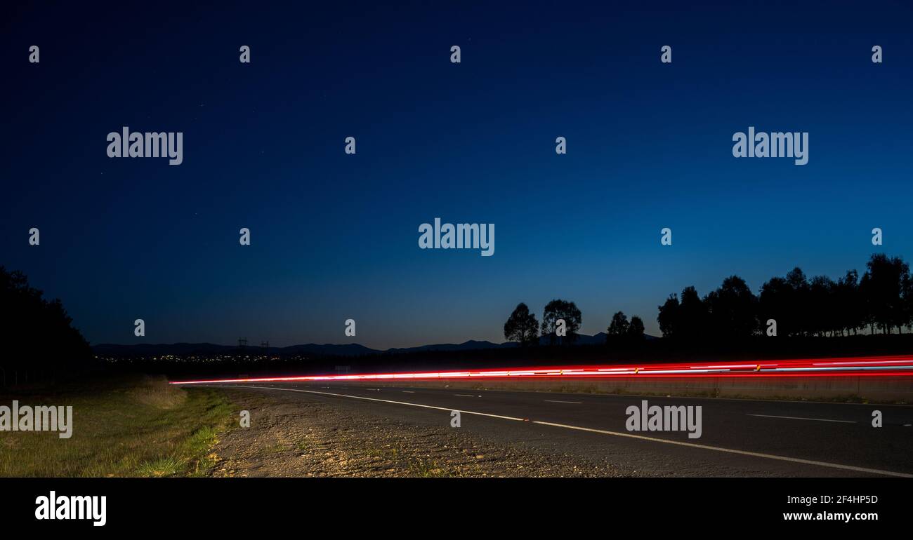 Light trail and Tuggeranong parkway highway in Canberra from the side of the road with sparkling stars and blue sky Stock Photo
