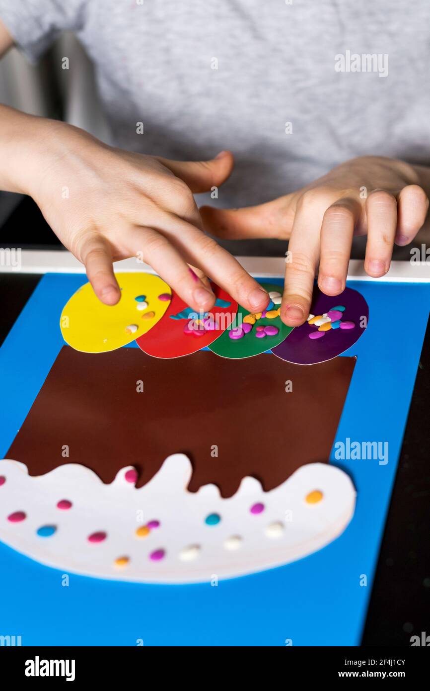 The boy makes an Easter card with his own hands, an Easter cake and Easter eggs from paper.  Stock Photo