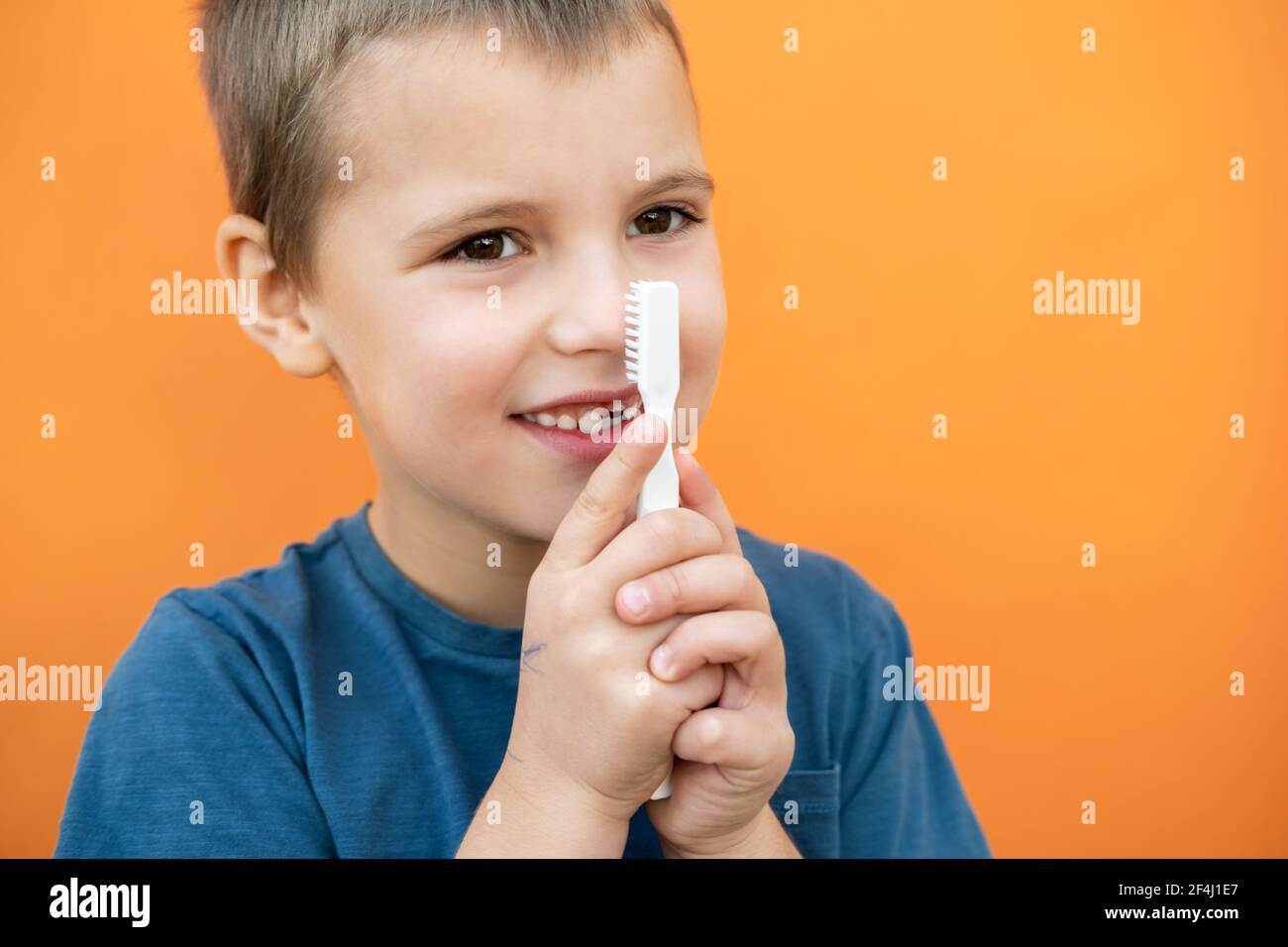 Boy without milk upper tooth in blue t-shirt holds toothbrush in hand on the orange background. Stock Photo