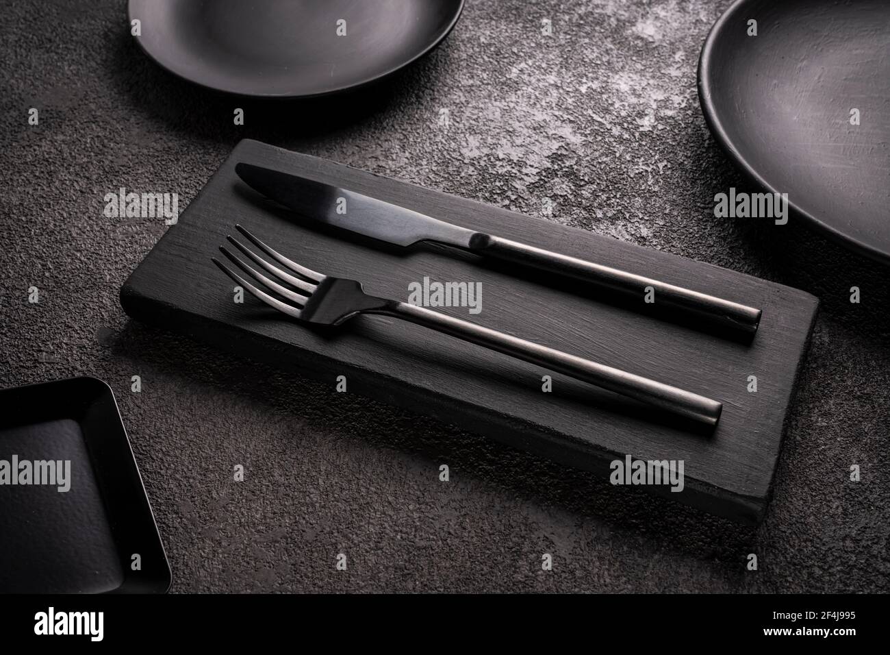 black table knife and fork surrounded by plates and dishes, close-up