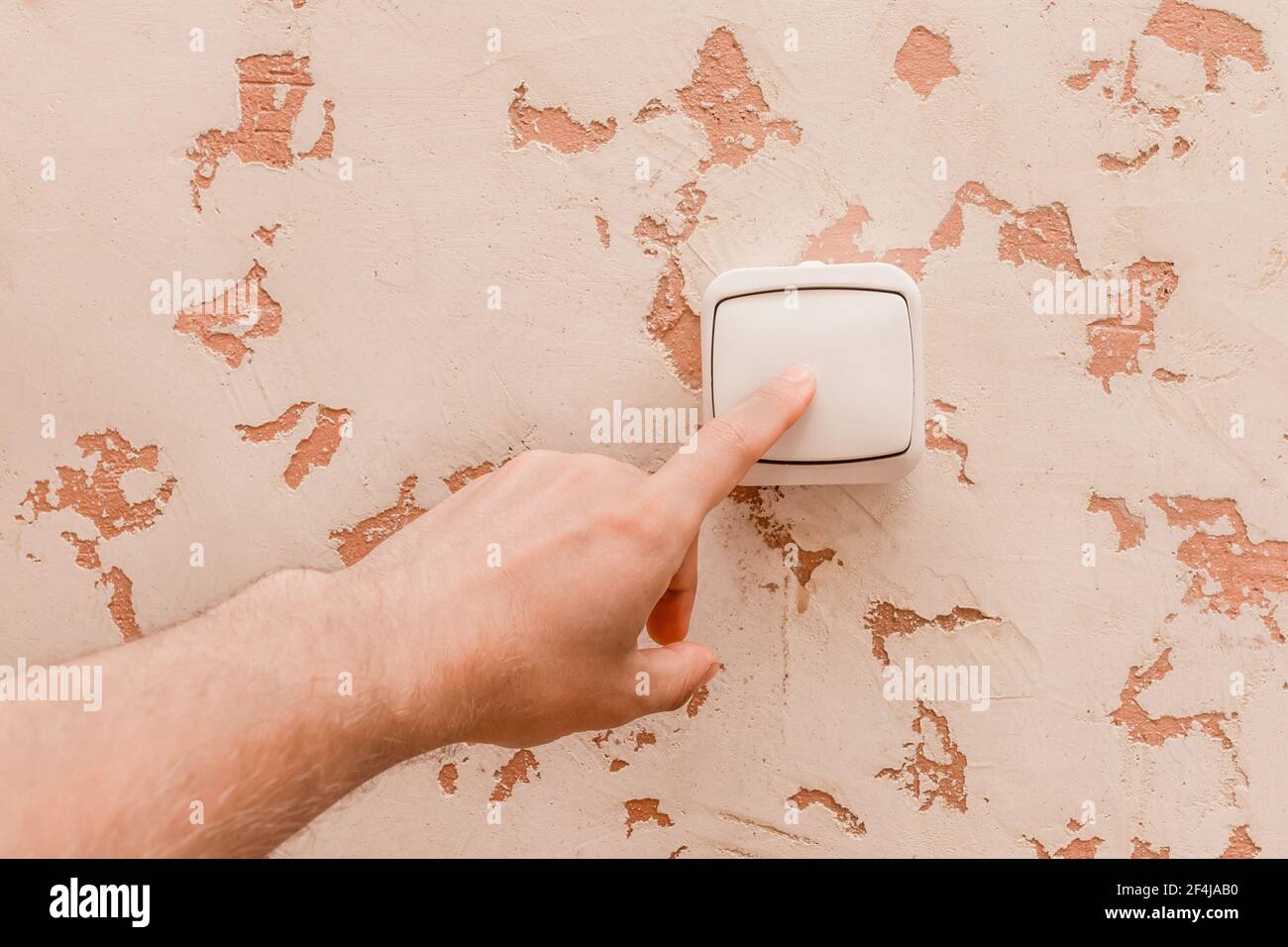 The guy's hand turns off the light with an electric switch in a modern room interior background. Stock Photo