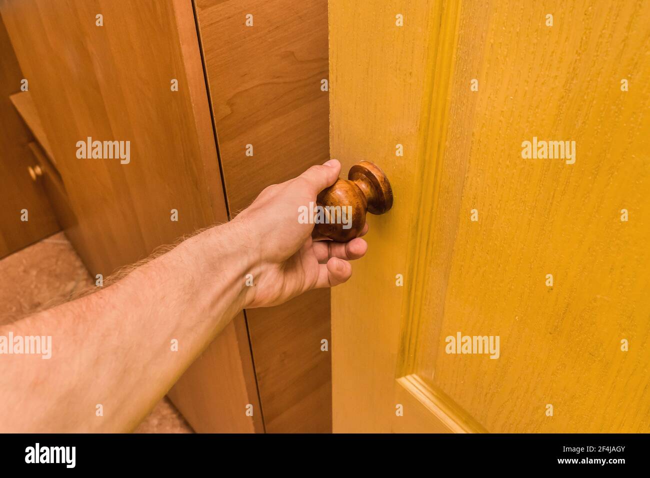 The guy's hand holds the handle and opens the yellow wooden door in the interior of the room. Stock Photo