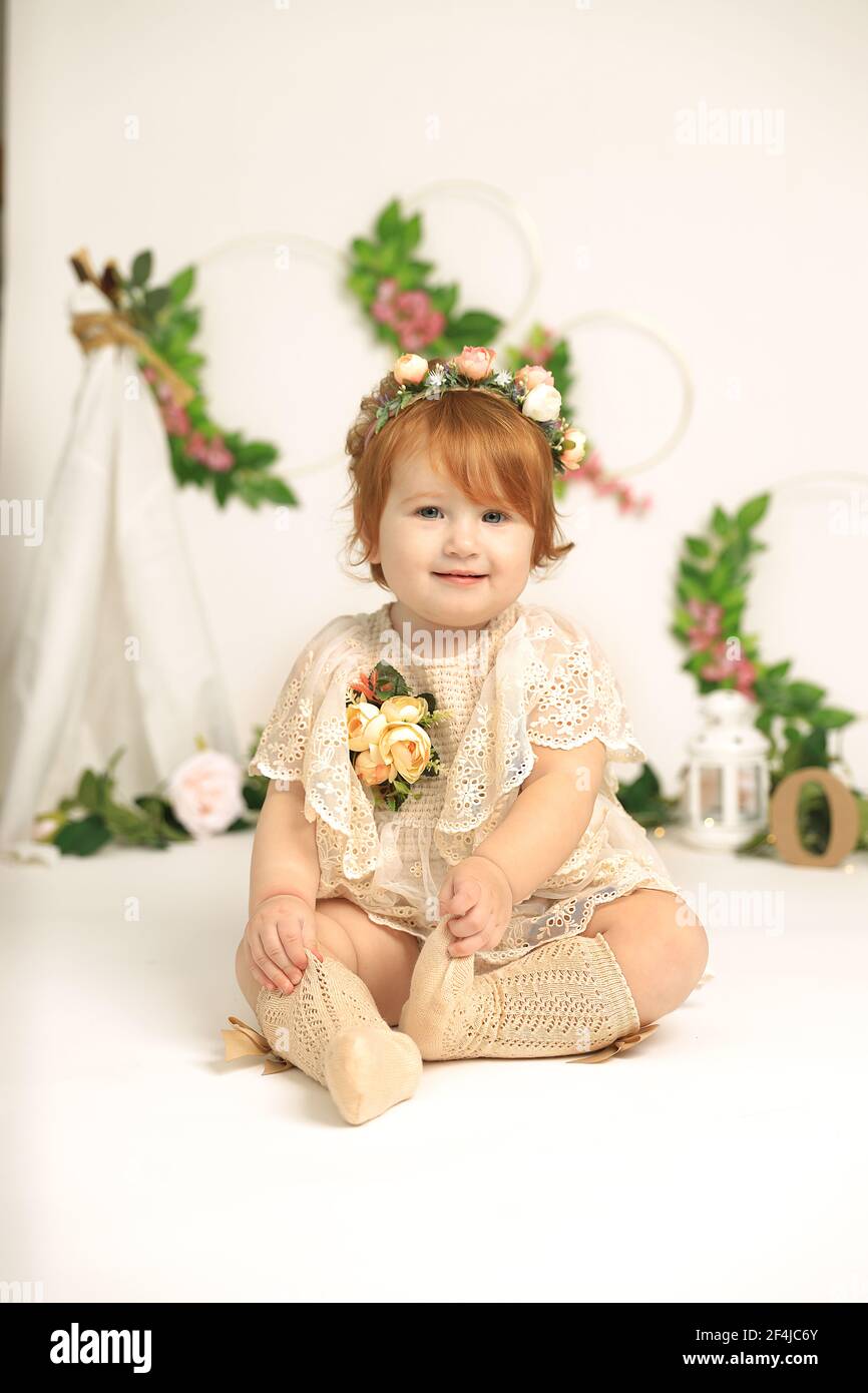 Little 1 years old red hair beautiful tender smiling girl, childhood celebration concept. Spring concept. Child in flowers. Studio photoshoot. Indoors Stock Photo