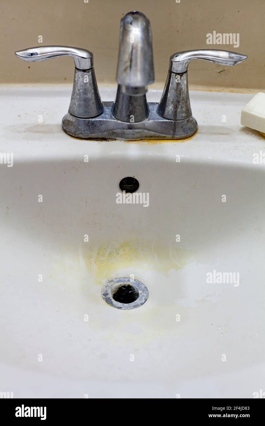 Close up image of a faucet and sink in a dirty bathroom. There are