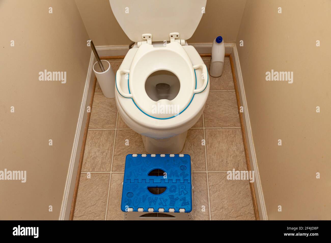 A child toilet seat attachment placed on top of a toilet for a kid during potty training. A step plastic stool is placed to help the kid get up to the Stock Photo