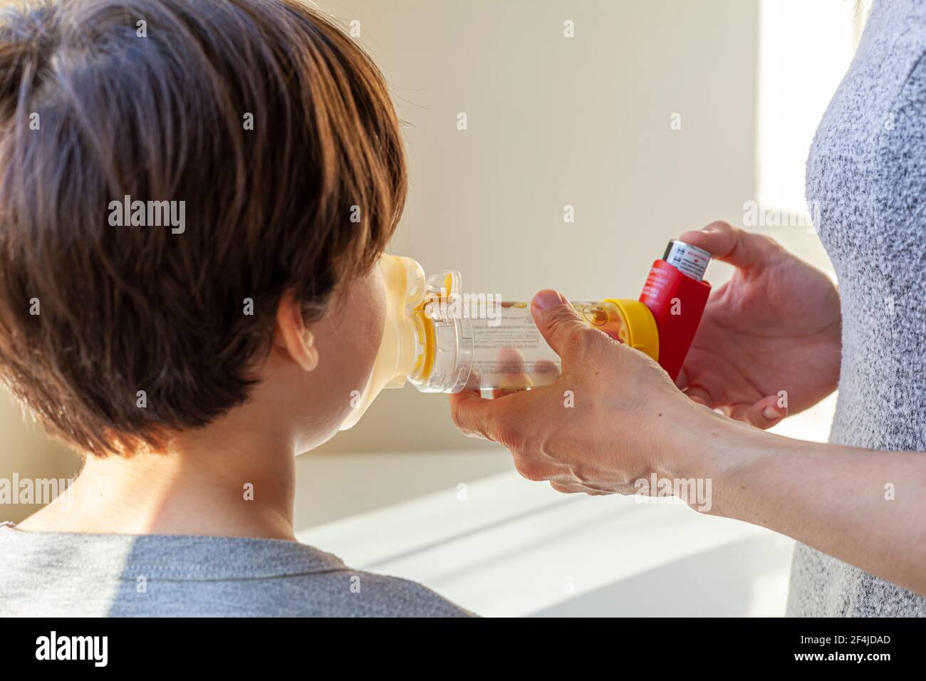 A caucasian woman is giving emergency asthma medication to a small kit during an attack. She uses aerosol chamber with valve mask to deliver bronchodi Stock Photo
