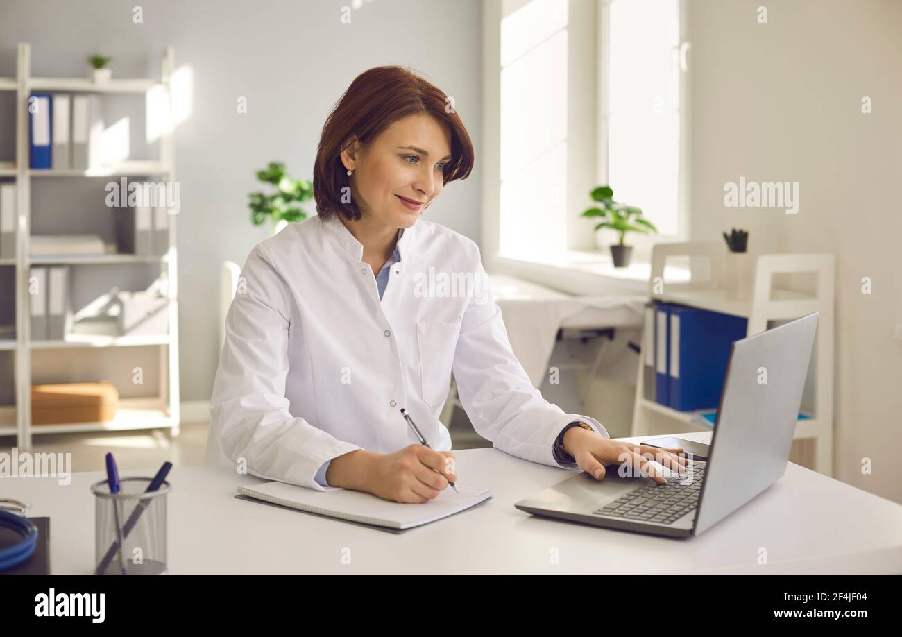 Female doctor writes notes while watching an online medical webinar or training seminar. Stock Photo