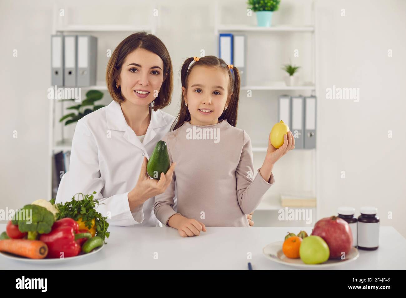 Nutritionist and little child at table with fresh vegetables, fruit and vitamins Stock Photo