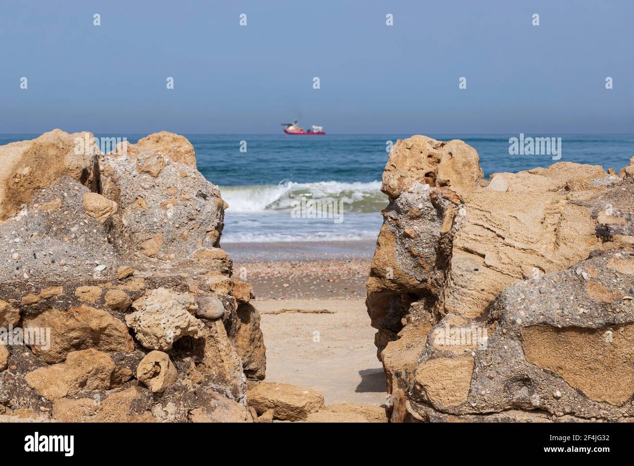 View of the Mediterranean Sea and the ship through the shell rock formations on the shore Stock Photo