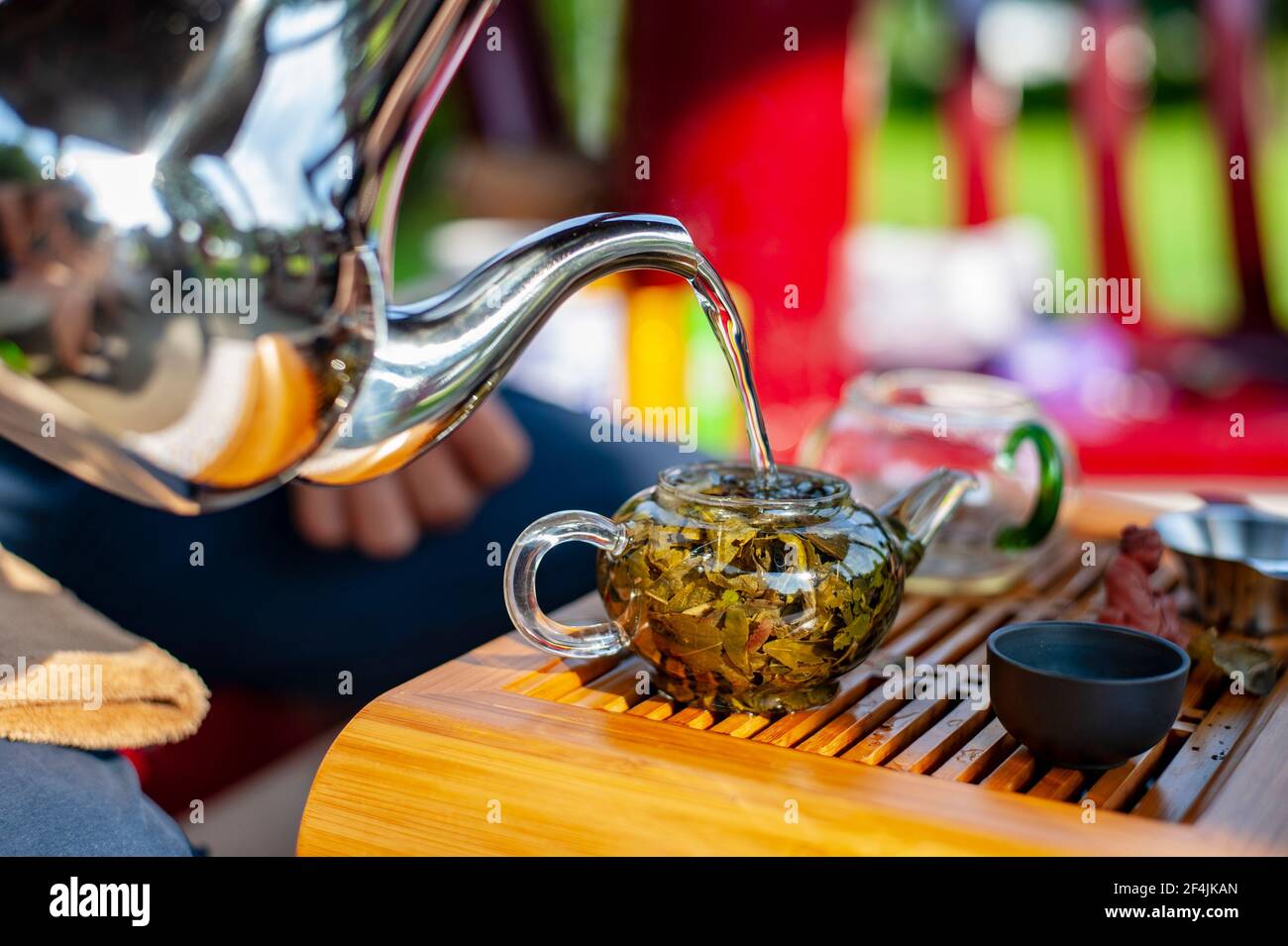Traditional Chinese tea ceremony. Hot water pouring into a glass teapot with green tea leaves of Chinese oolong tea in it. Stock Photo