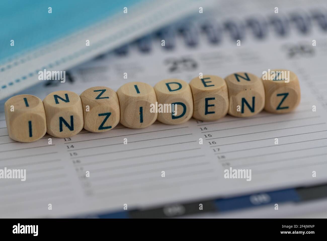 closeup of the german word for incidency (Inzidenz) on wooden cubes on a calendar with a surgical mask in the background Stock Photo