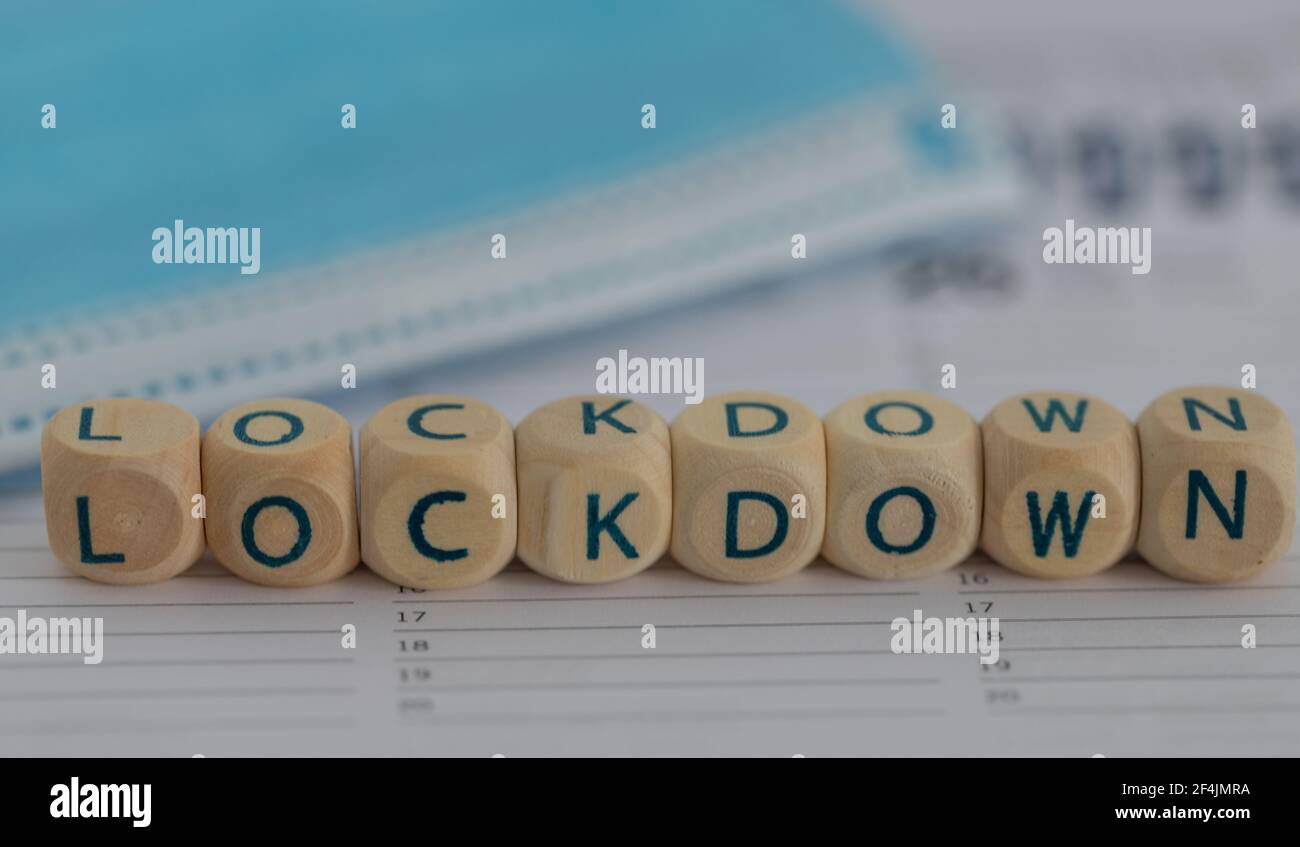closeup of the word lockdown on wooden cubes on a calendar with a surgical mask in the background Stock Photo