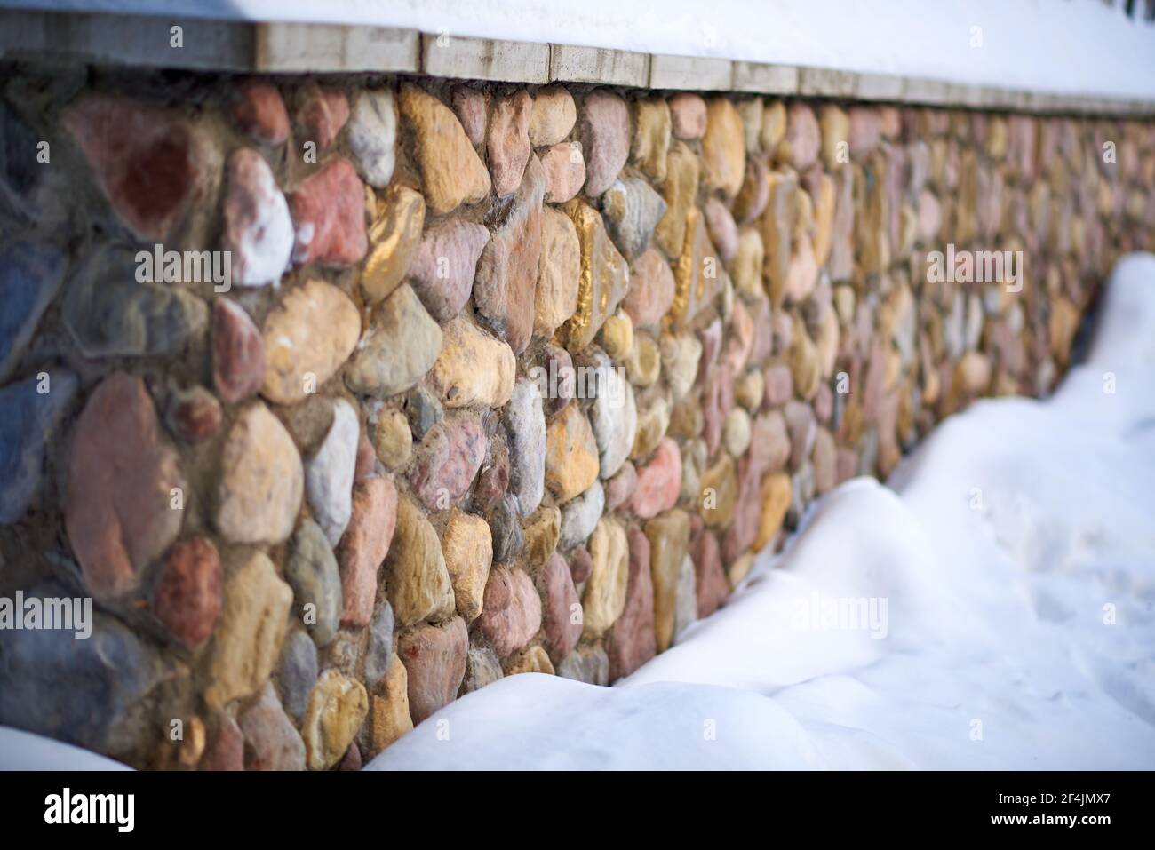 Wall decorated with multi-colored decorative stone. Down below the snow Stock Photo