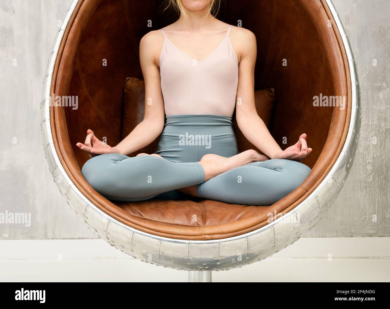 Anonymous woman meditating in the lotus Pose in a leather chair in a close up view of her crossed legs and hands in a health and fitness and relaxatio Stock Photo