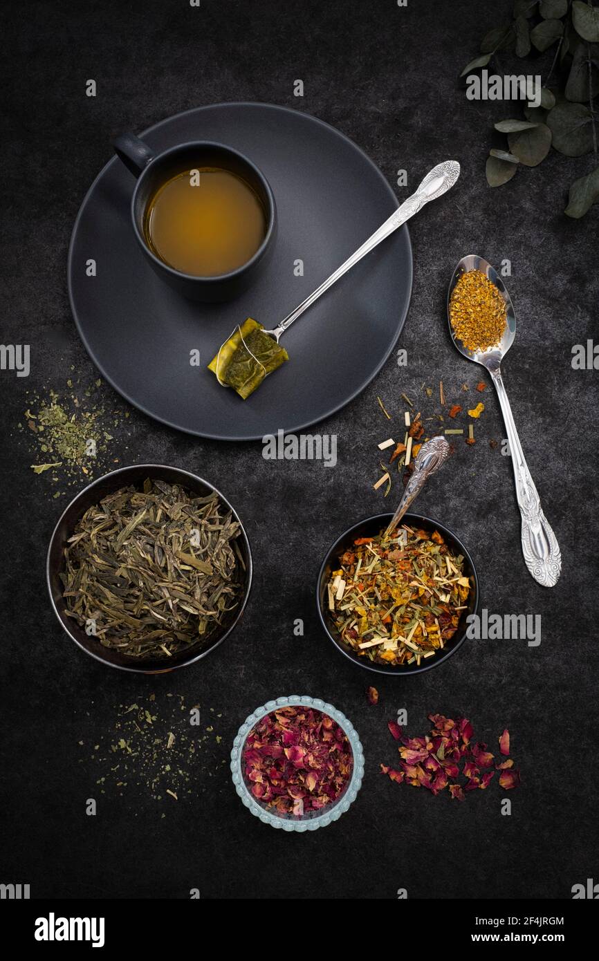 A black cup of turmeric tea with various cups of tea herbs on a black surface Stock Photo